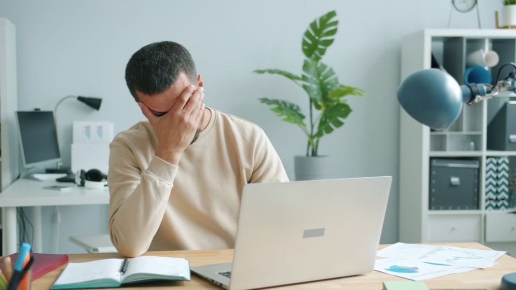 Frustrated worker in front of his laptop with his hands covering his face