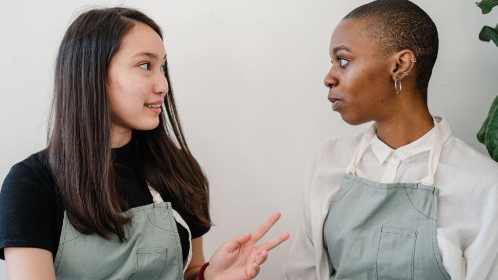 Two female workers wearing an apron talking to each other