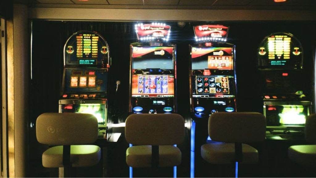 Slot machines in a dimly lit casino with reflective ceiling and empty chairs