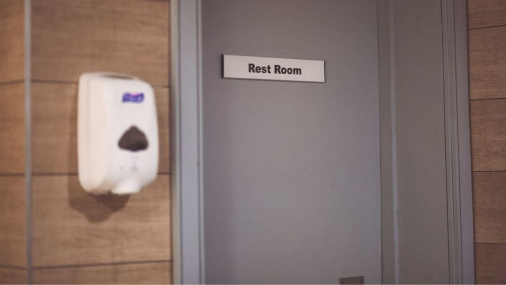 A restroom door with a label in front and a sanitizer dispenser on the side