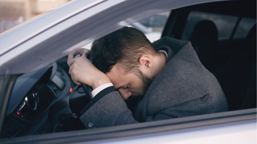 Man feeling tired wiht his head on the car's steering wheel