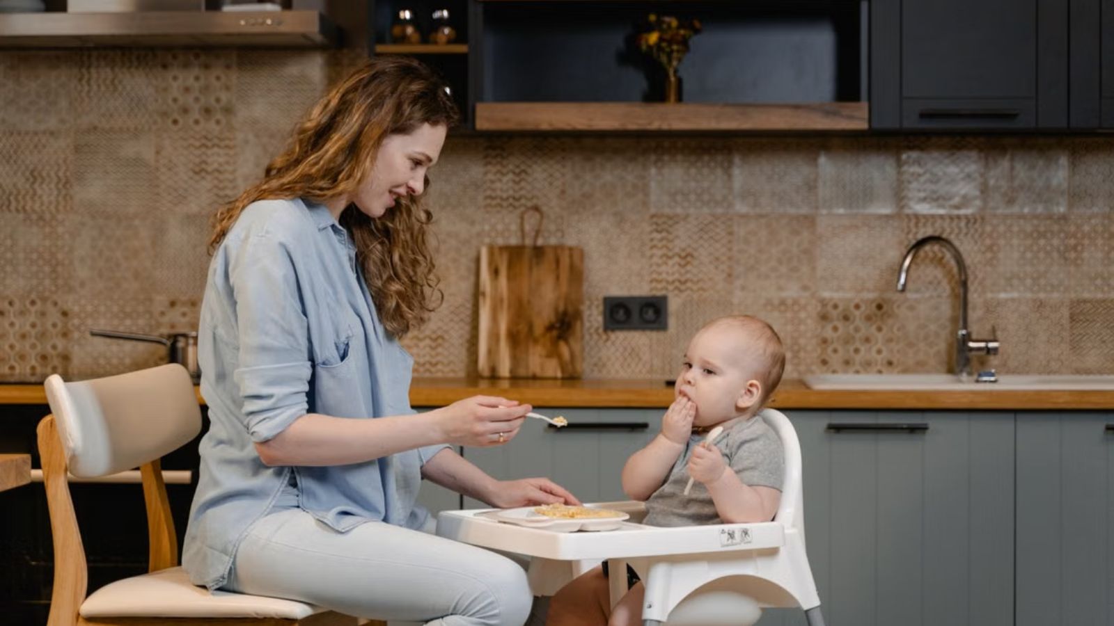 Woman feeding her baby who's sitting on a high chair