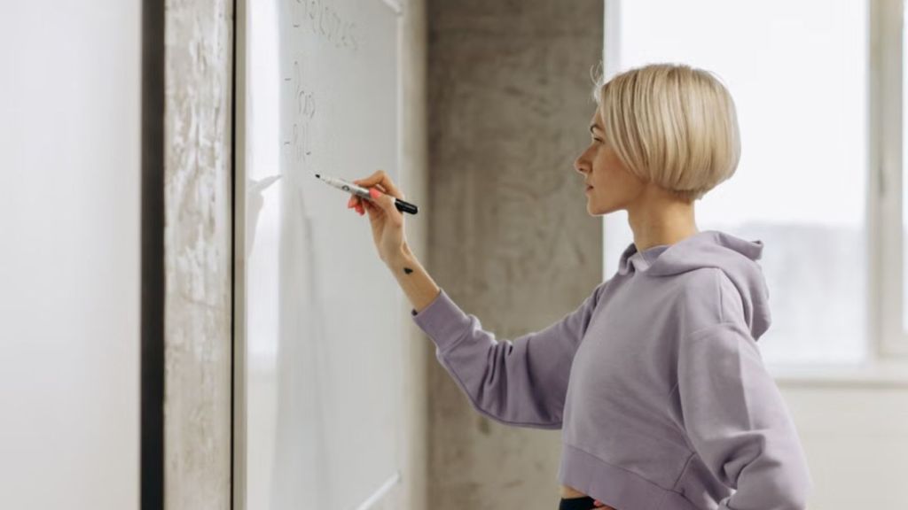Woman writing with a marker on the whiteboard mounted on the wall