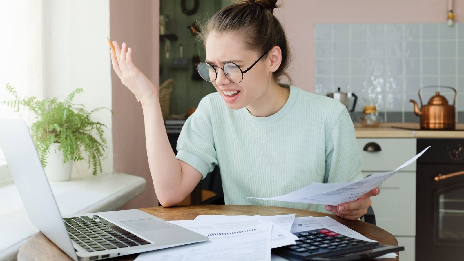 upset young woman looking at bills and laptop