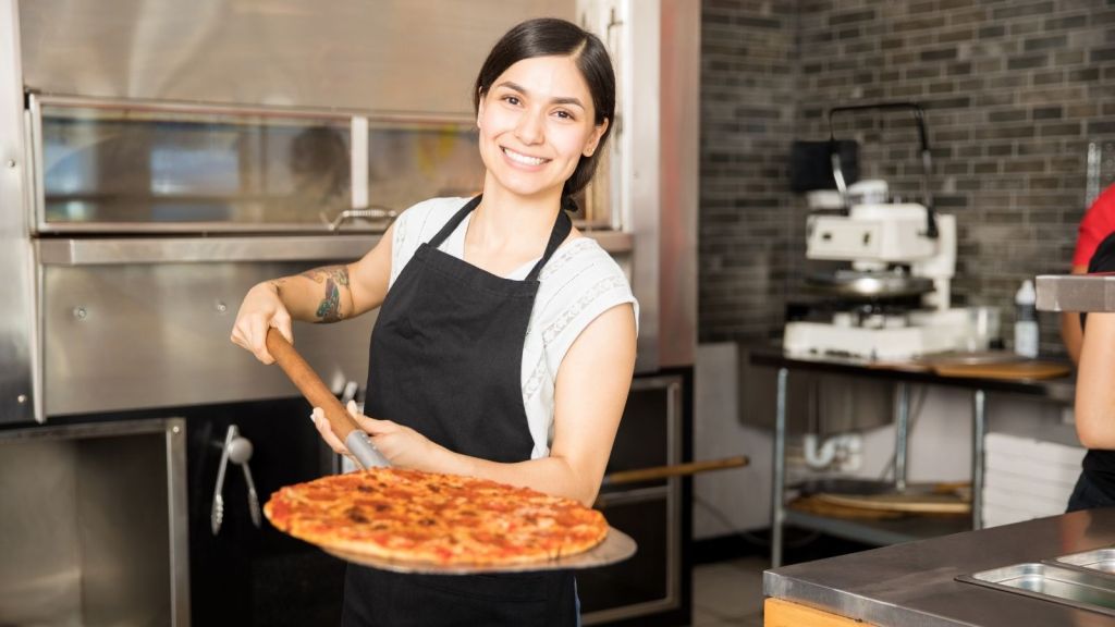 smiling woman holding a pizza on a pizza peel