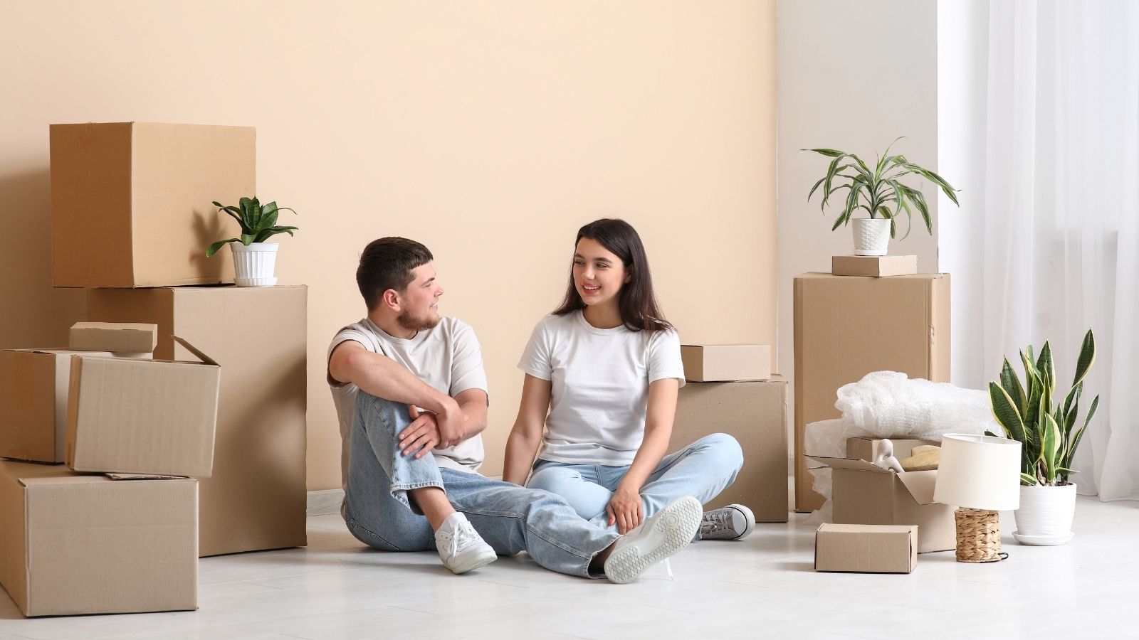 Couple Says Early Move Out Fee Feels Unfair After Job Opportunity Forces Them to Leave couple sitting on the floor surrounded by moving boxes