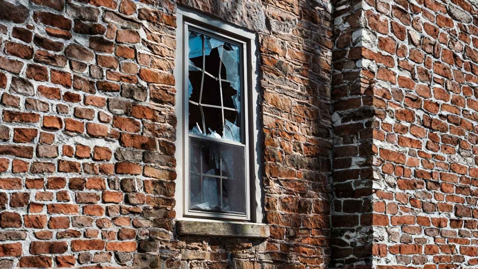 Toy School Bus Nearly Smashes Homeowner’s Window During Backyard Baseball Game, Prompting an Immediate Decision closeup of broken window on brick house
