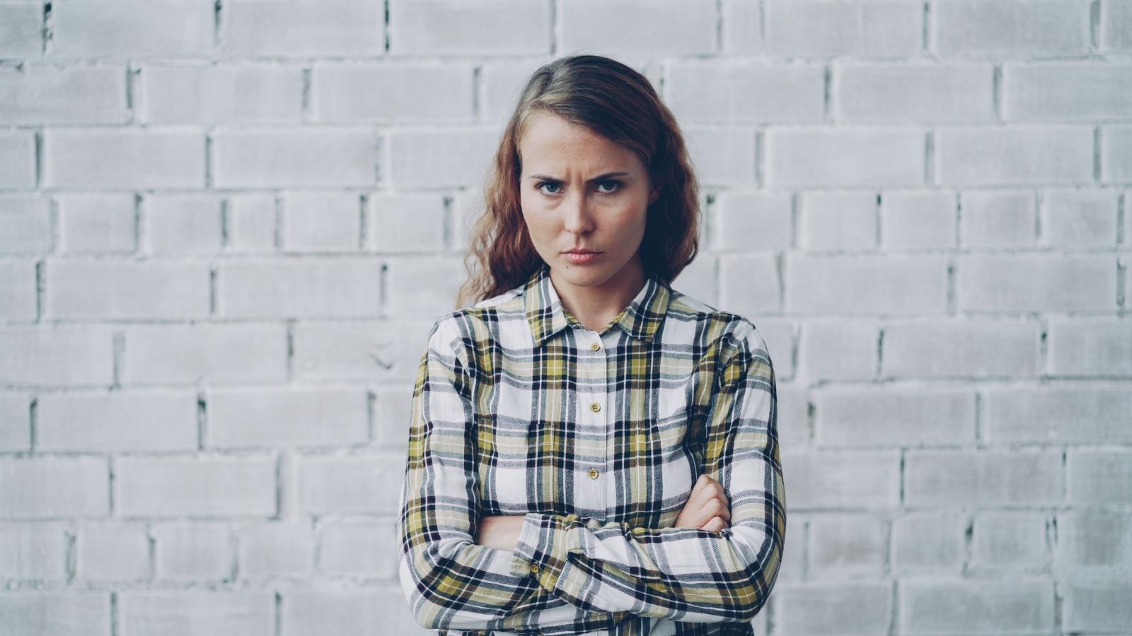 She Just Wanted to Clarify Her Onboarding Paperwork. Inside the Terrifying Moment a Senior Colleague Threw an Absolute Tantrum. upset woman in plaid crossing arms against brick wall