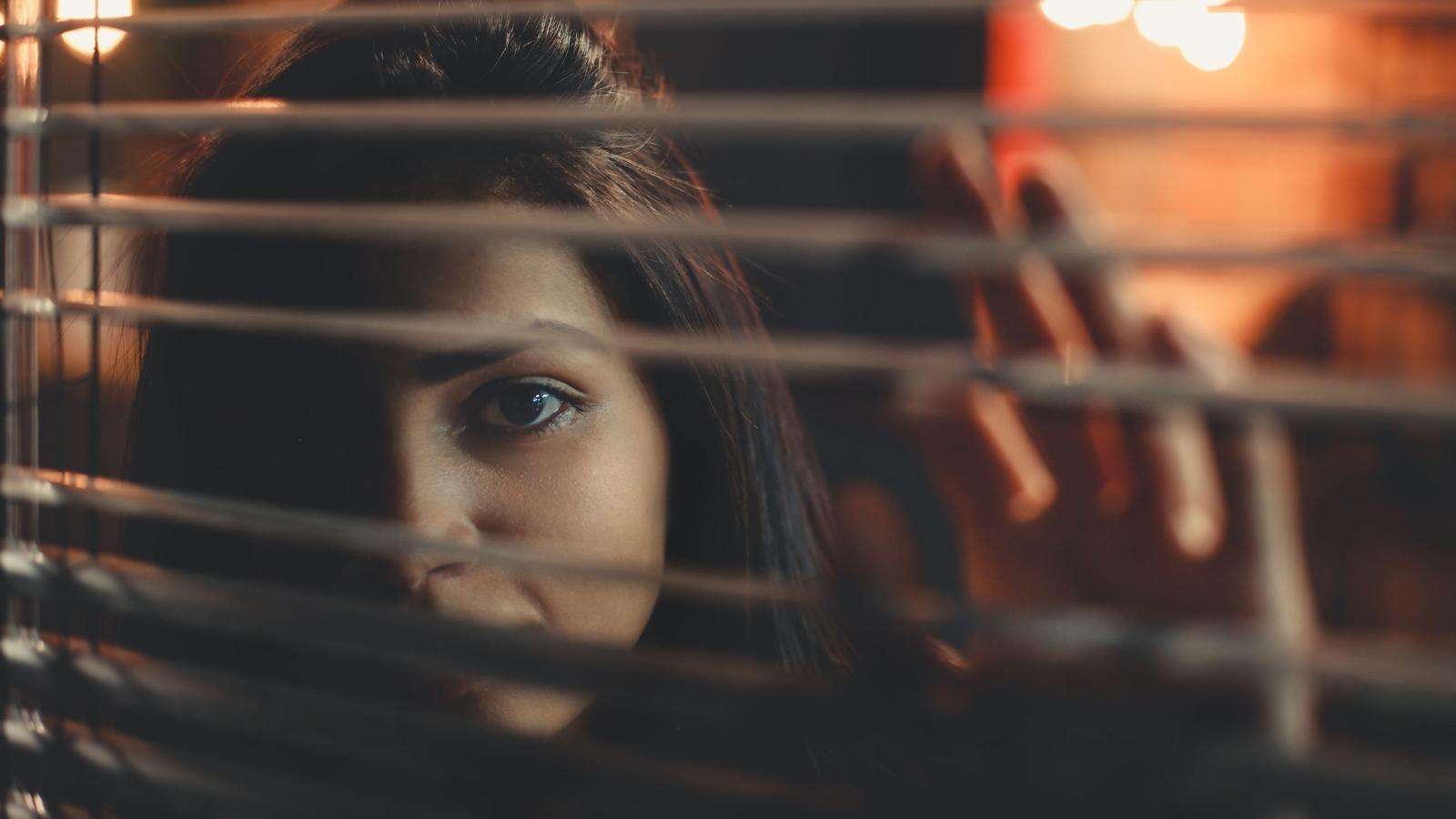 She Lives in a Cul De Sac and Cant Avoid Her Neighbors House — Every Walk Turns Into a Mandatory 30 Minute Chat woman looking through her window blinds