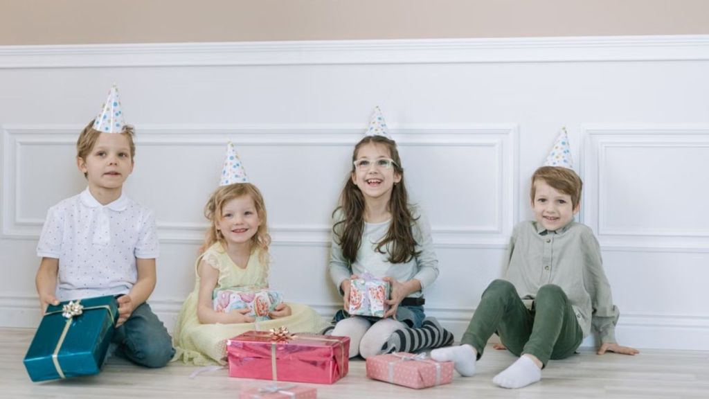 Children with party hats happily sitting on the floor with gifts