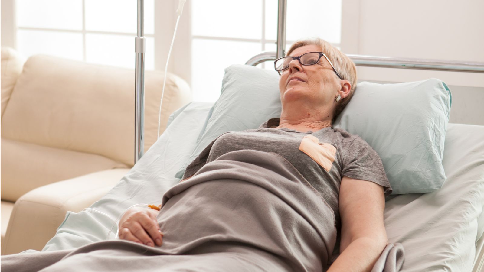 She Thought Her Mom’s Surgery Went Great—Then Her Dad Lashed Out Over Her Selfish Lack of Check Ins Middle aged woman lying in hospital bed with dextrose attached to her