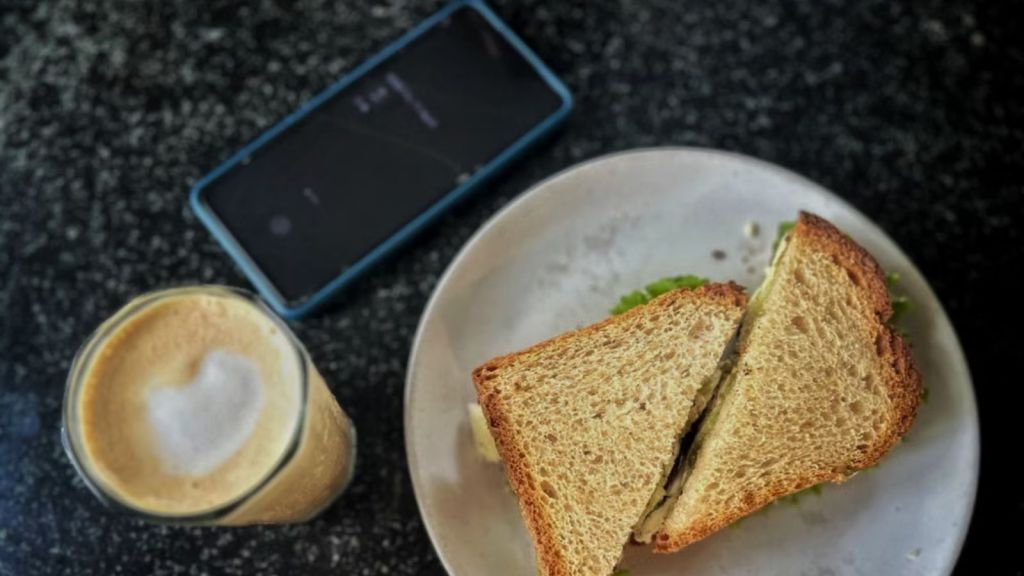 Sandwich and coffee laid on the table with a mobile phone