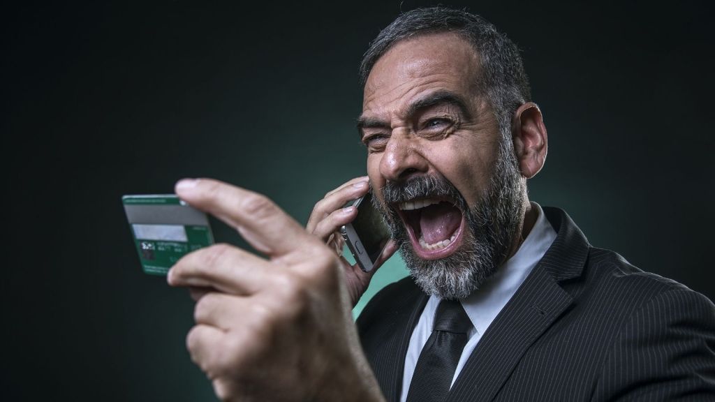angry older man holding a credit card and yelling in a phone