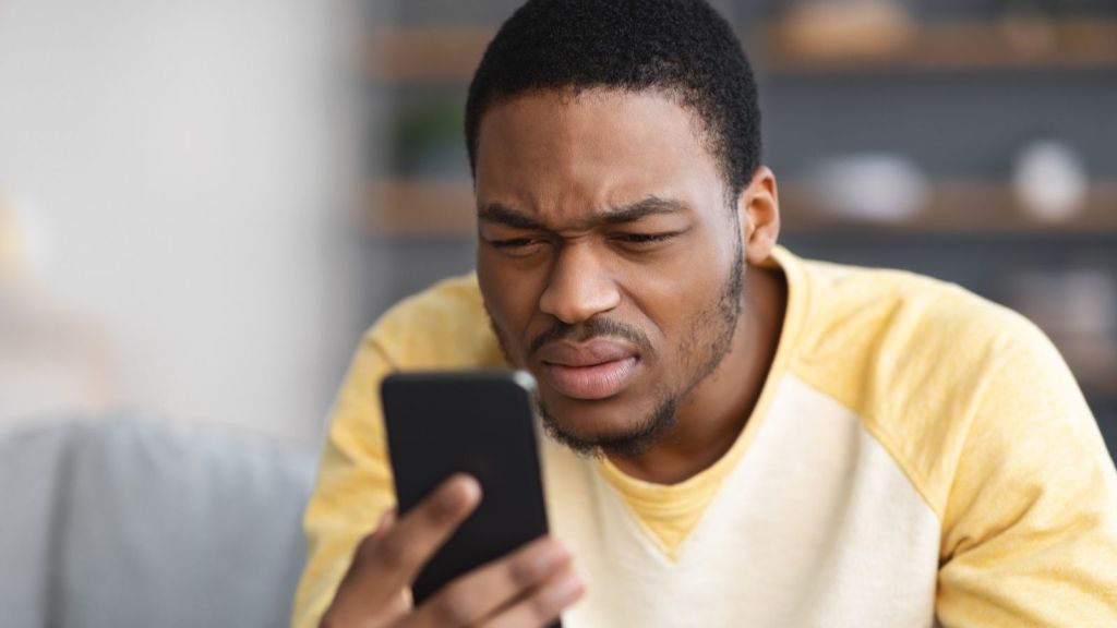 man squinting while looking at his phone