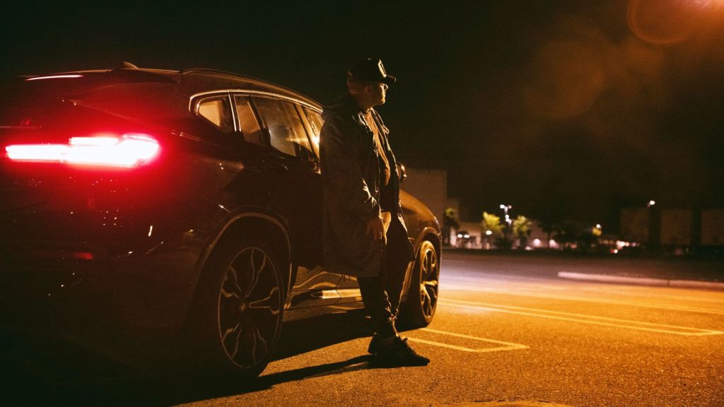 Man leaning abck on a parked car in the street at night time