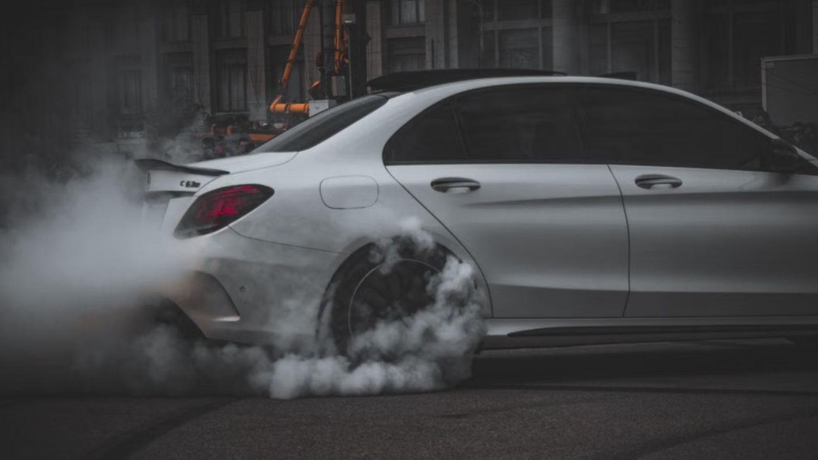 He Laughs in My Face Every Morning: Woman Outraged After Confronting Neighbor Over Loud Car White car performing a dramatic drift, emitting smoke on a dark asphalt surface