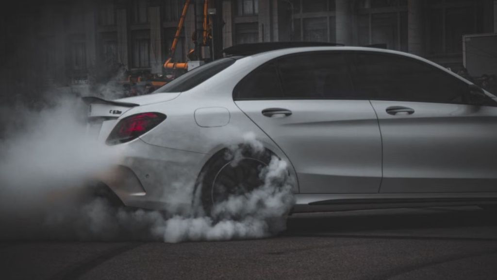 White car performing a dramatic drift, emitting smoke on a dark asphalt surface