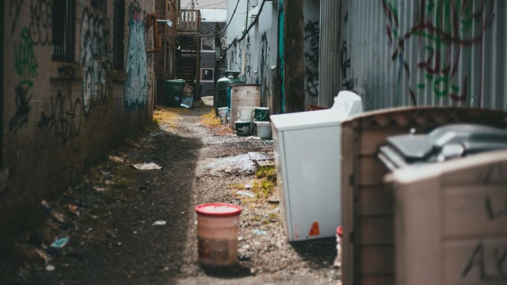 A narrow urban alley filled with scattered trash and graffiti-covered walls