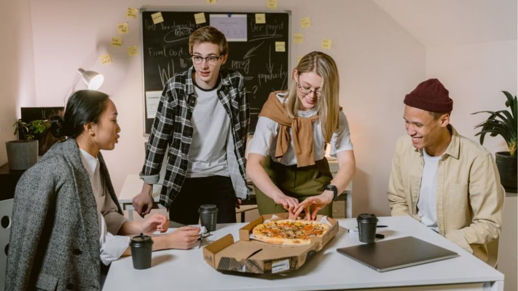 Employees in casual work attire sharing a box of pizza in the office