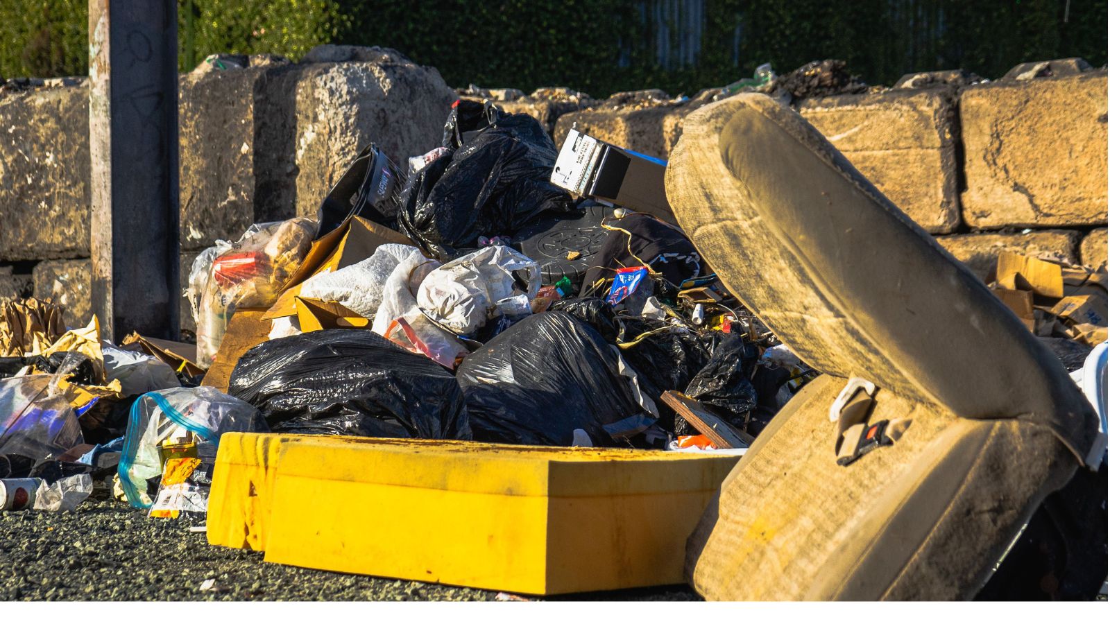 Outdoor scene of a garbage pile including a discarded mattress and various waste materials