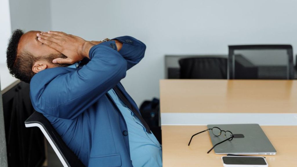 Man feeling bored at work and covering his face with his hands