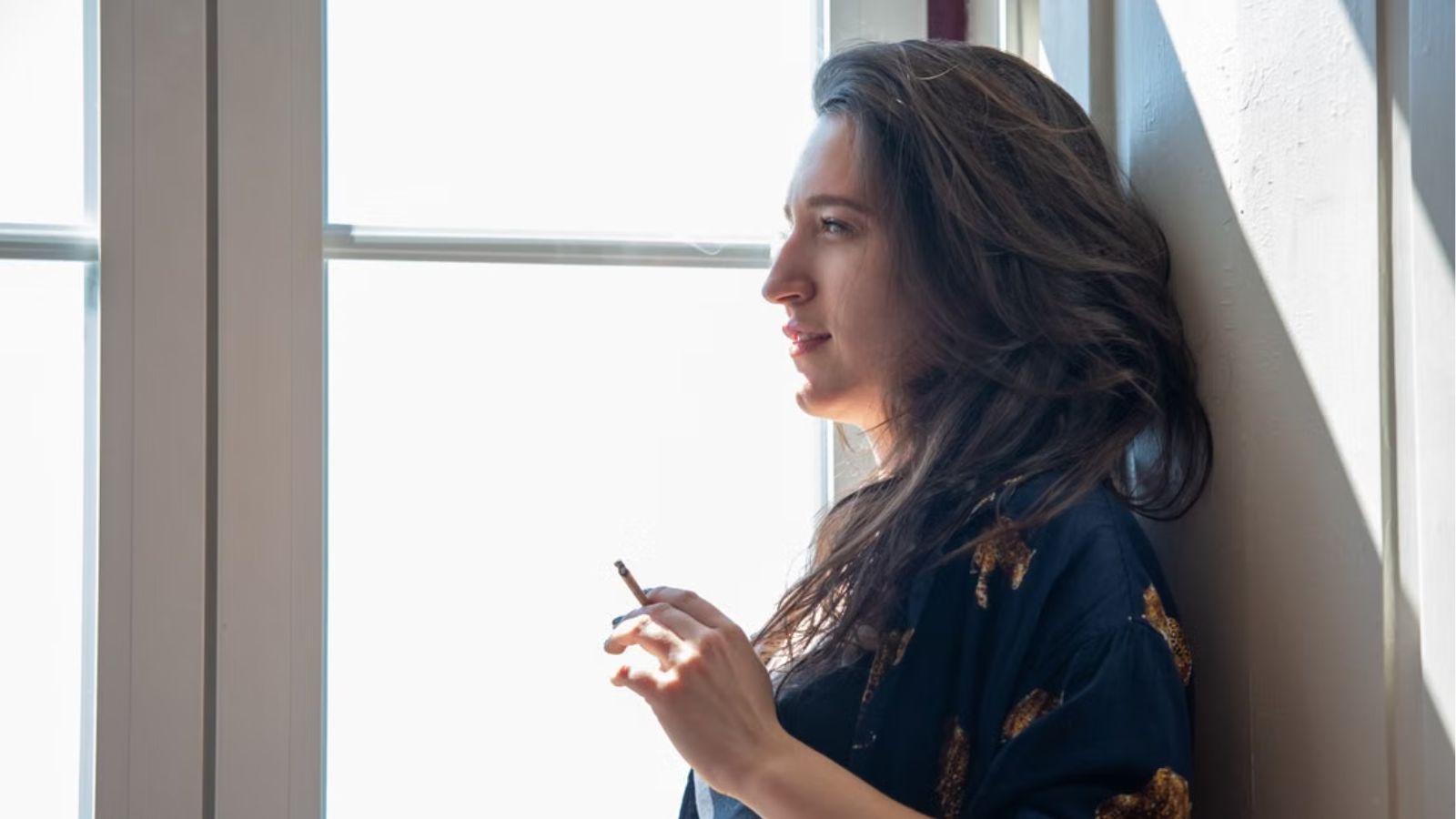 He Confronted His Neighbor About Smoking in Their Shared Enclosed Space—But Instead of Stopping, She Accused Him of Shaming and Harassing Her, Leaving Him to Wonder if Raising a Health Concern Made Him the Bad Guy Woman holding a cigarette and smoking near the window