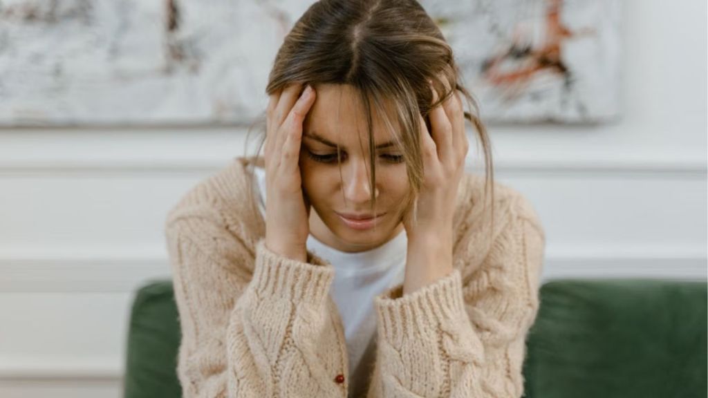 Woman sitting on a sofa holding her head, expressing stress and frustration indoors