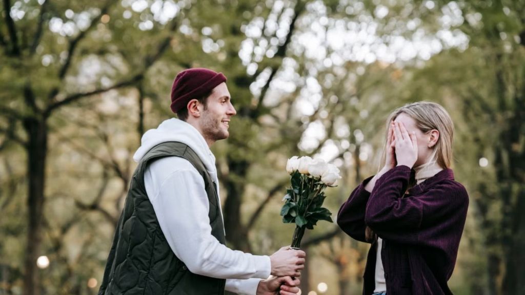 Man handing flowers to a woman who is covering her face with her hands