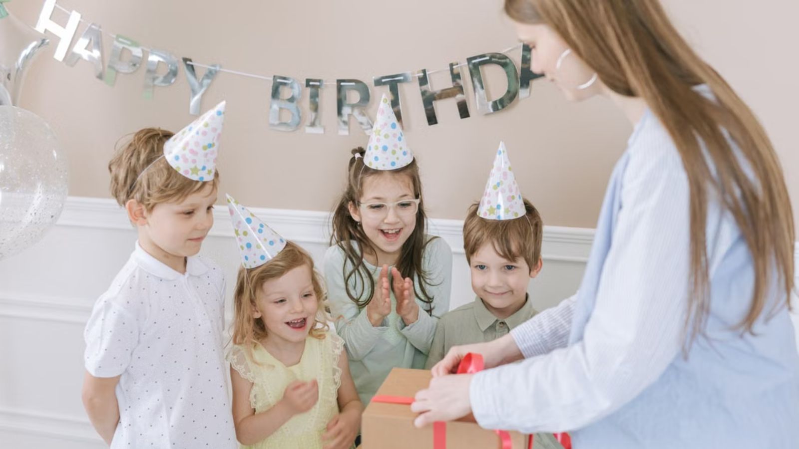 Happy children wearing party hats eagerly await a gift at a birthday party
