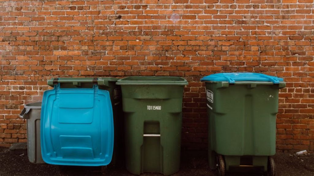 Three garbage bins placed in front of a rustic brick wall in an urban setting