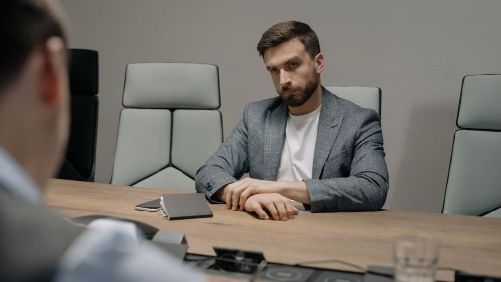 An employee with a serious face and in business attire sitting in a conference room