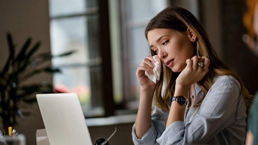Young woman quietly weeping in front of her laptop in the office
