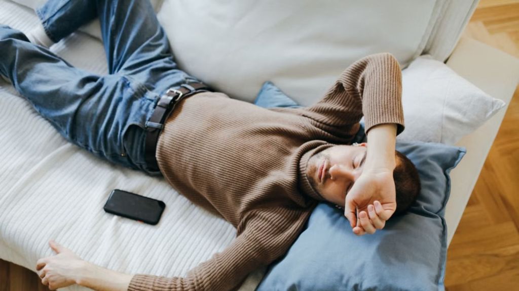 Exhausted man lying on a couch with his phone beside him