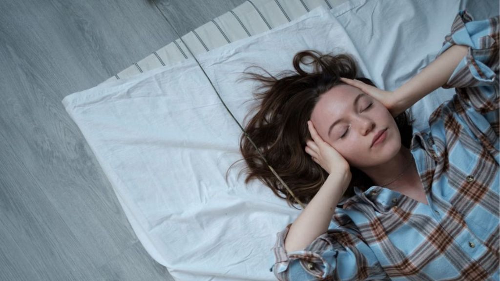 Woman lying on the floor with eyes closed and her hands covering her ears