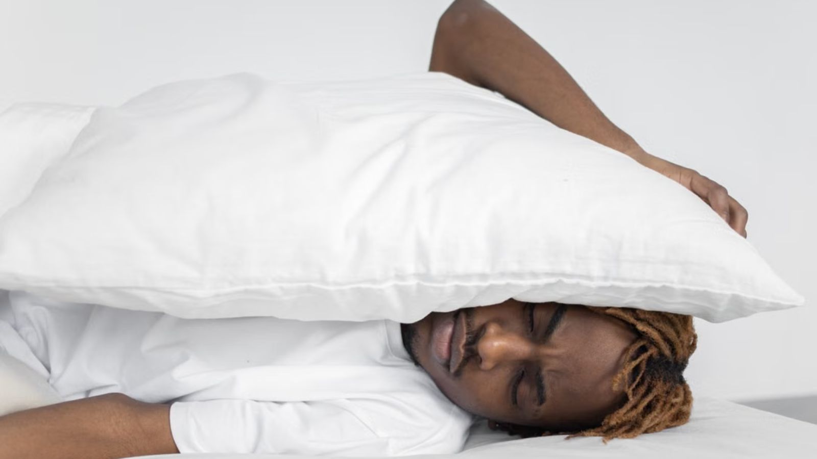 He Just Wanted to Study and Sleep in His Hostel Room. His Roommates Wouldnt Let Him. Man covering his ear with a pillow because he can't sleep with the noise