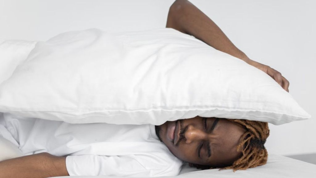 Man covering his ear with a pillow because he can't sleep with the noise