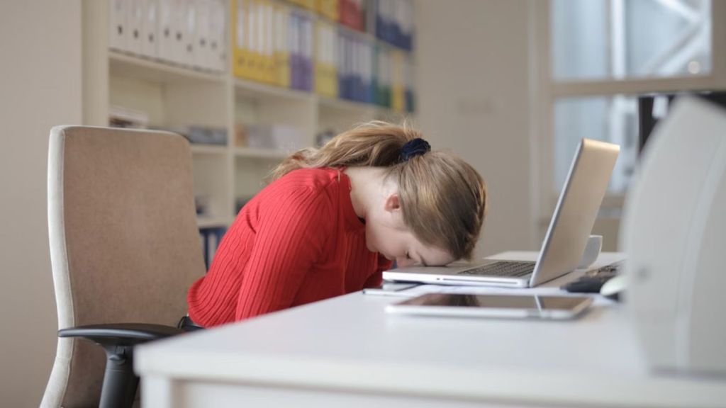 Woman feeling miserable at work with her head resting on the desk with a laptop