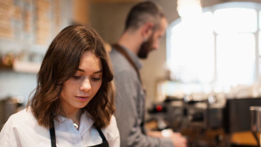 Young woman and man wearing apron and working in a cafe