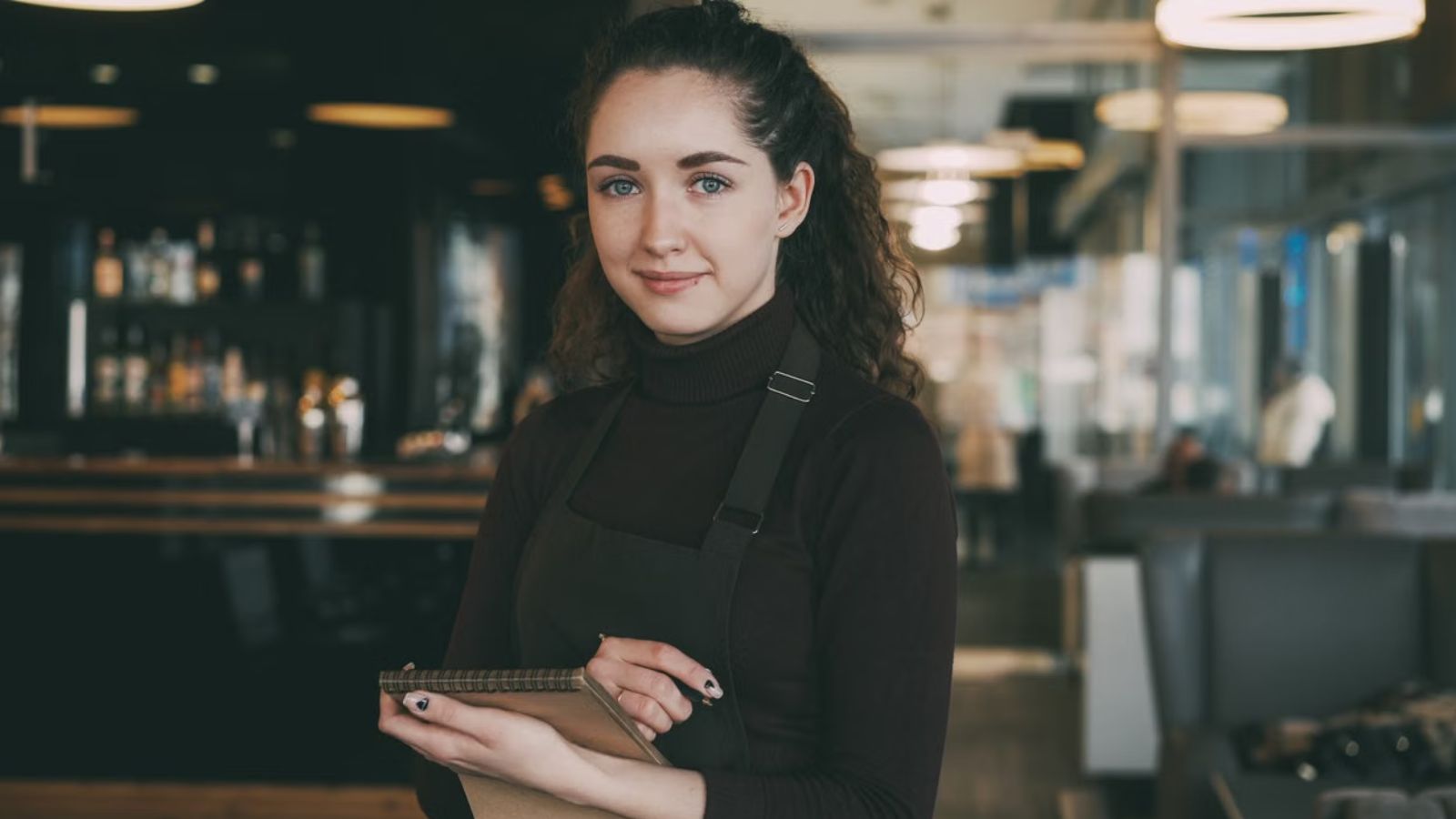 She Tried to Seat Hotel Guests at a Quieter Table—Until Her Coworker Yelled at Her for Extra Work Waitress smiling while holding a notebook in a restaurant