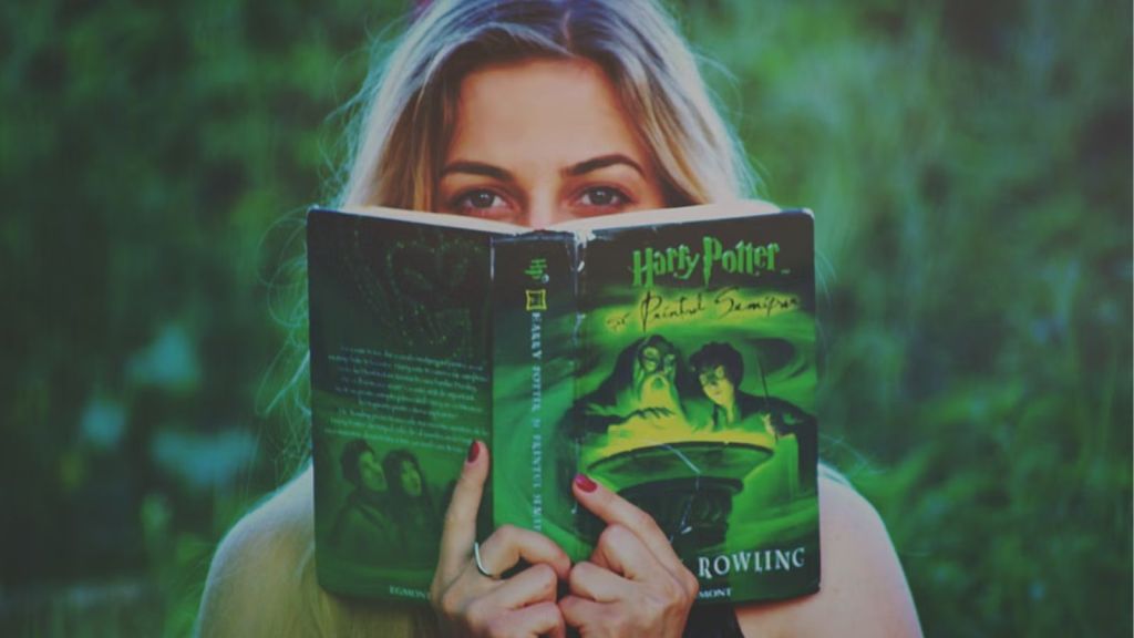 Woman reading a Harry Potter book with a green, outdoorsy background
