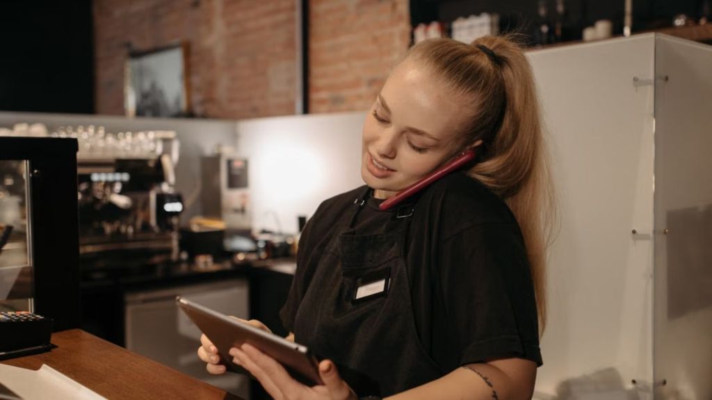 Employee talking to someone on the phone while using a tablet in a cafe