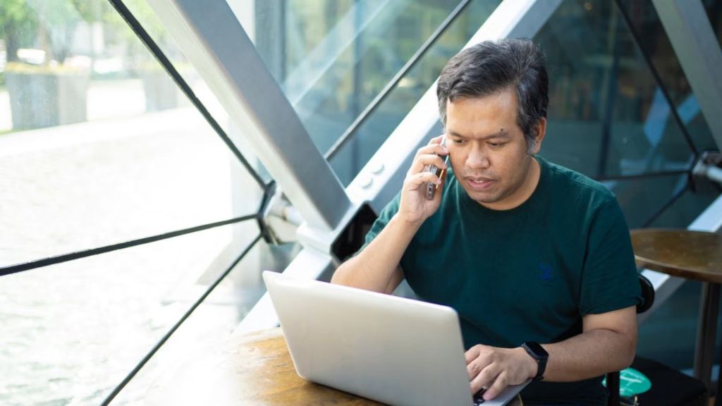 Man talking on his phone while looking at his laptop screen