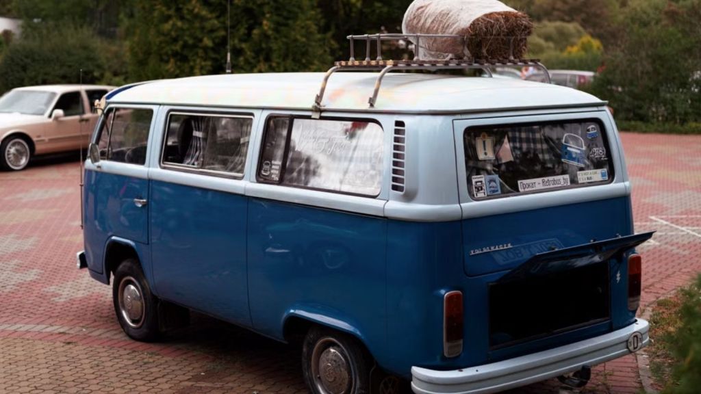 A vintage blue camper van parked in an outdoor setting with luggage on the roof rack