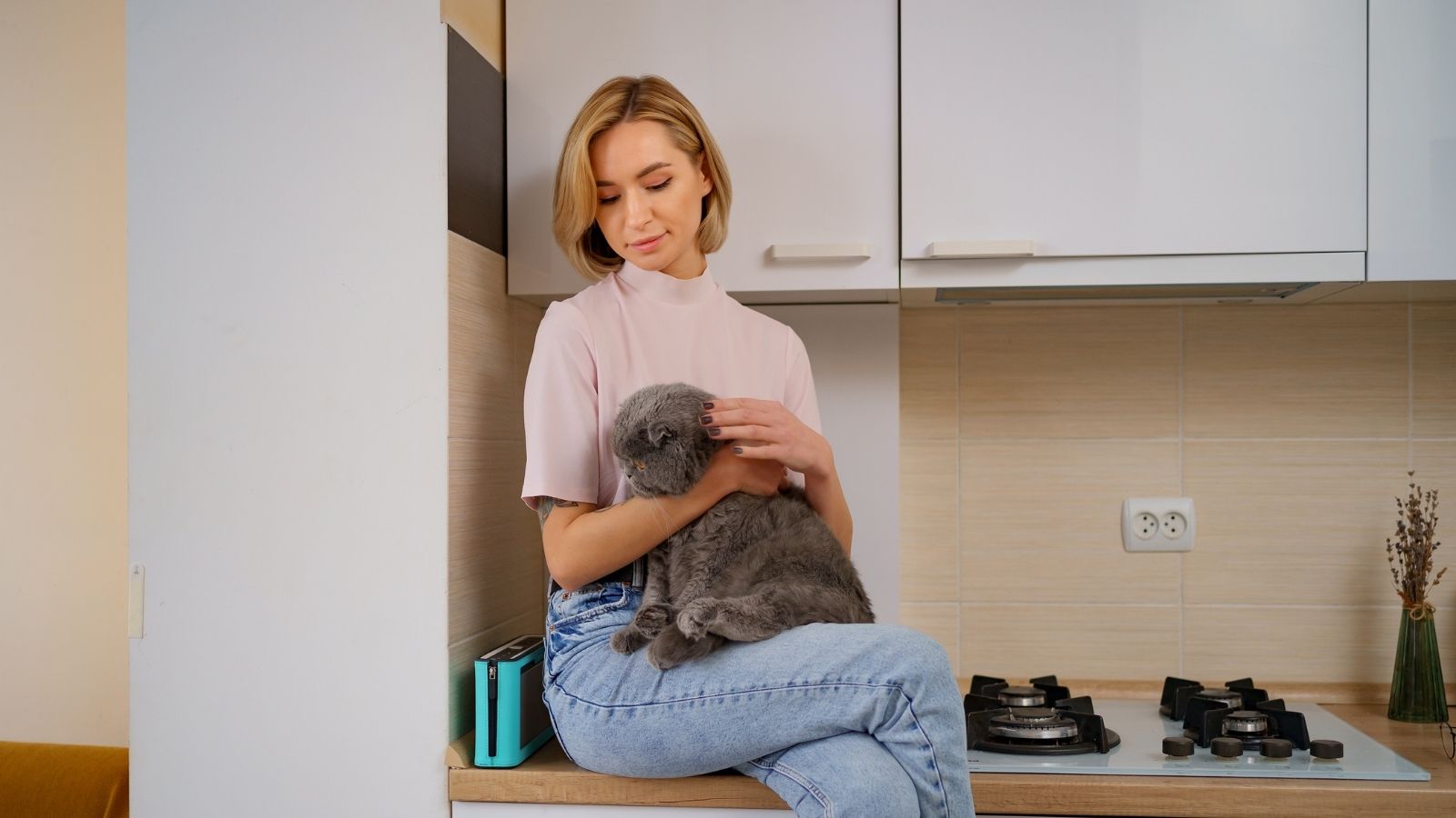 Woman sitting on the kitchen counter while cuddling her fluffy black cat