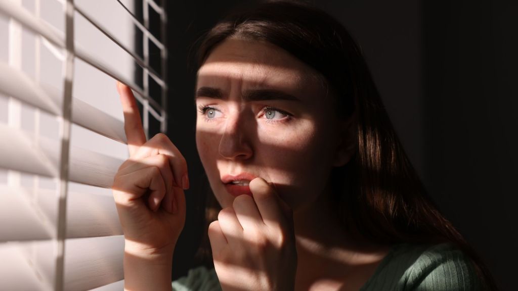 scared woman peeking through the blinds