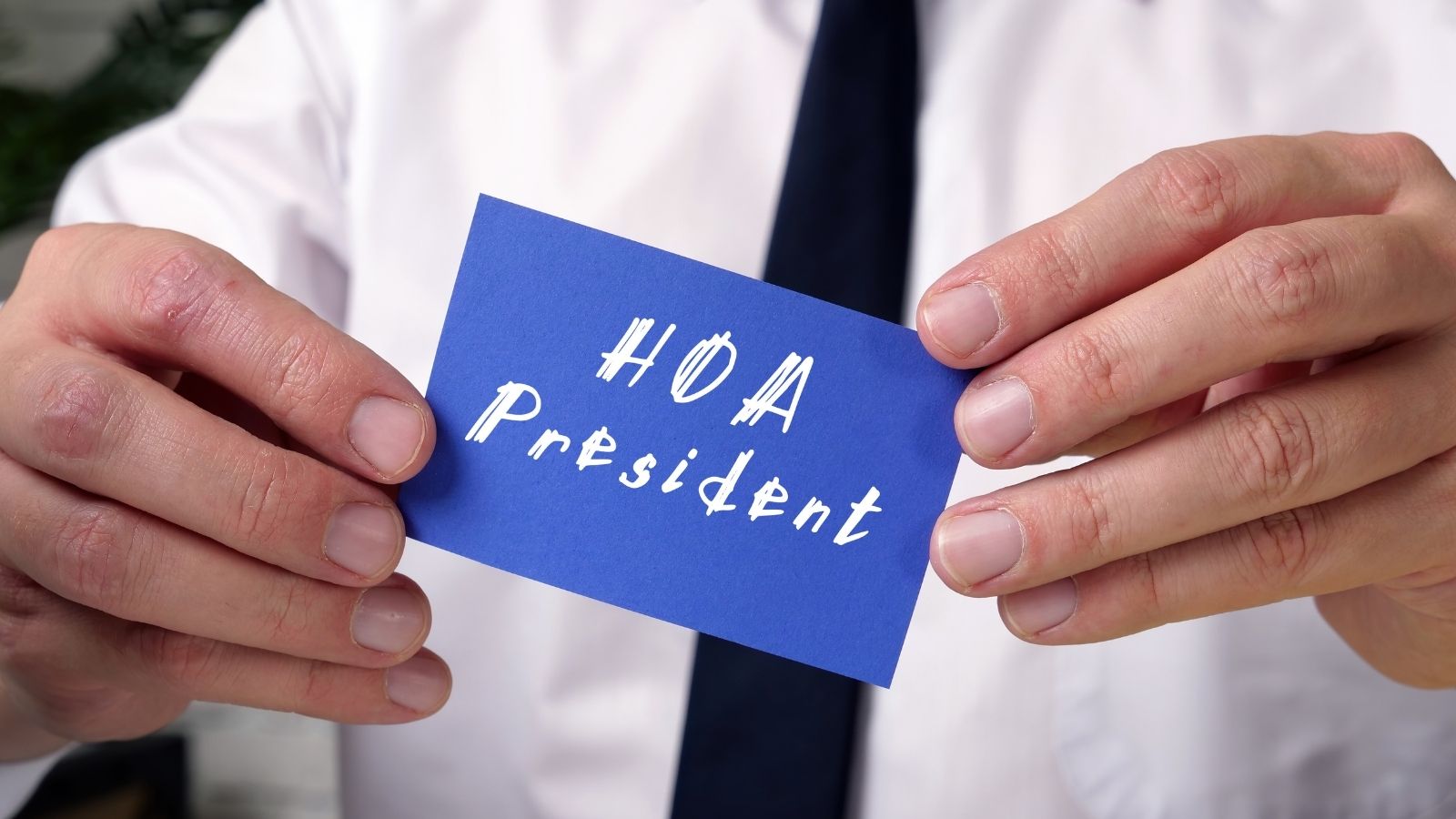 He Joined the HOA Board to Get Rid of It—Now He Has to Enforce the Rules He Hates man holding a blue card that reads "HOA President"