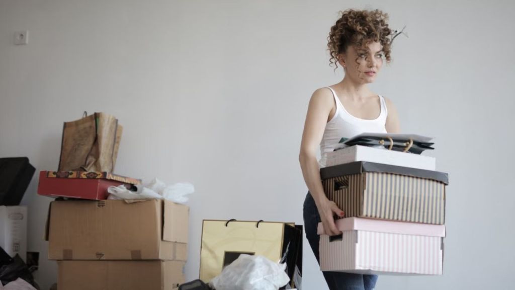 Woman carrying boxes of her things while other messy stuff is on the floor