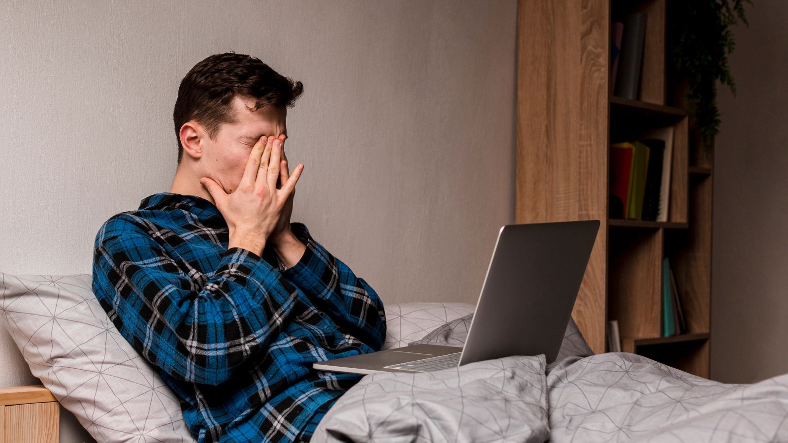 He Thought College Housing Would Be Exciting—Then His Roommates Made It Miserable Young man trying to finish work but feeling sleepy in bed
