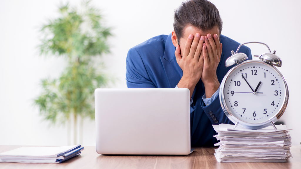 One Worker Raised An Obvious Problem With Being Assigned To Multiple Locations At Once, But His Manager Refused To Offer Any Real Solution businessman at his desk with large clock and face in his hands