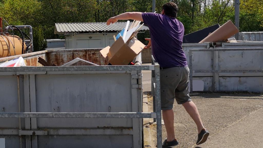 man throwing box into a dumpster